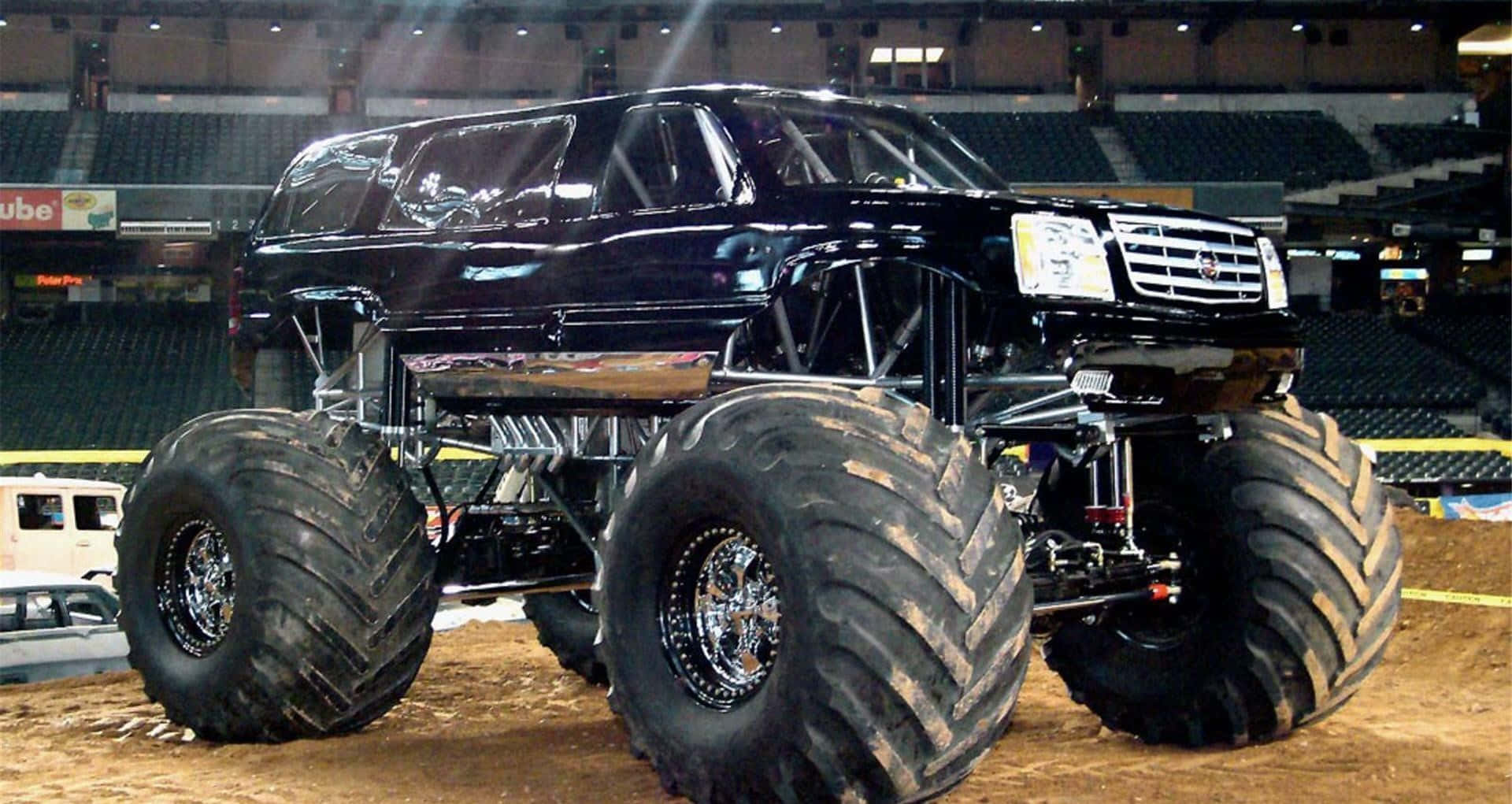 A Black Monster Truck With Large Tires On The Ground