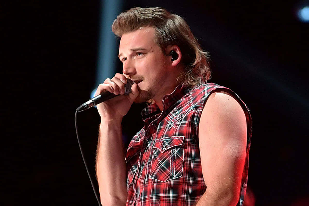 A Man In A Plaid Shirt Singing Into A Microphone