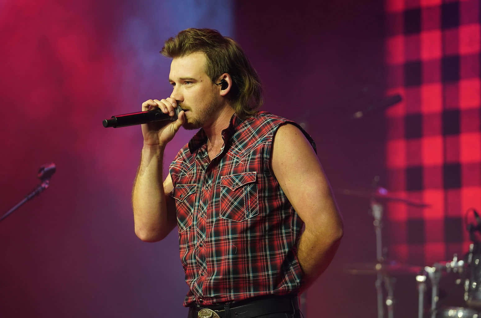 A Man In A Plaid Shirt Singing Into A Microphone