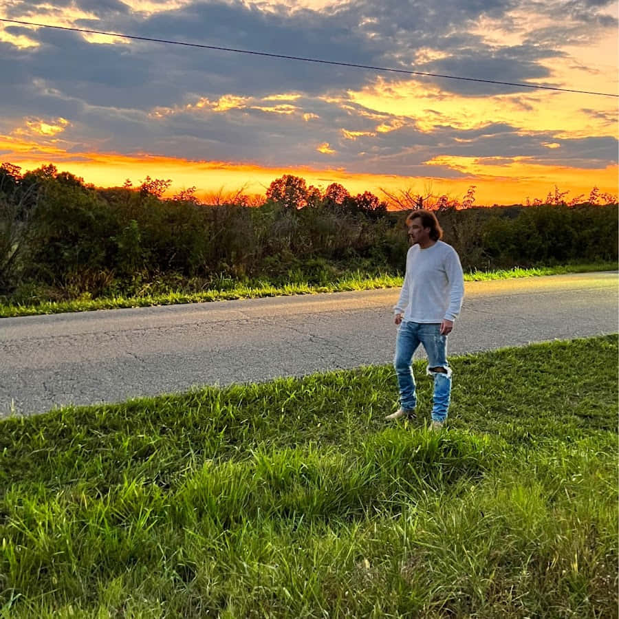 A Man Standing On The Side Of A Road At Sunset