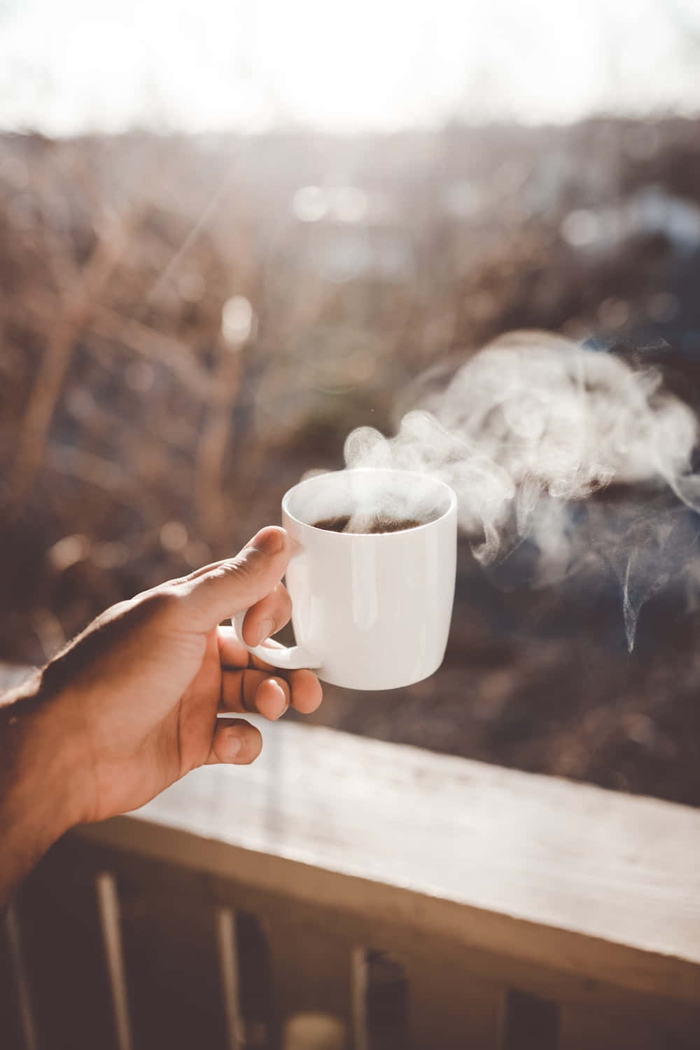 A Hand Holding A Cup Of Coffee With Steam Coming Out Of It