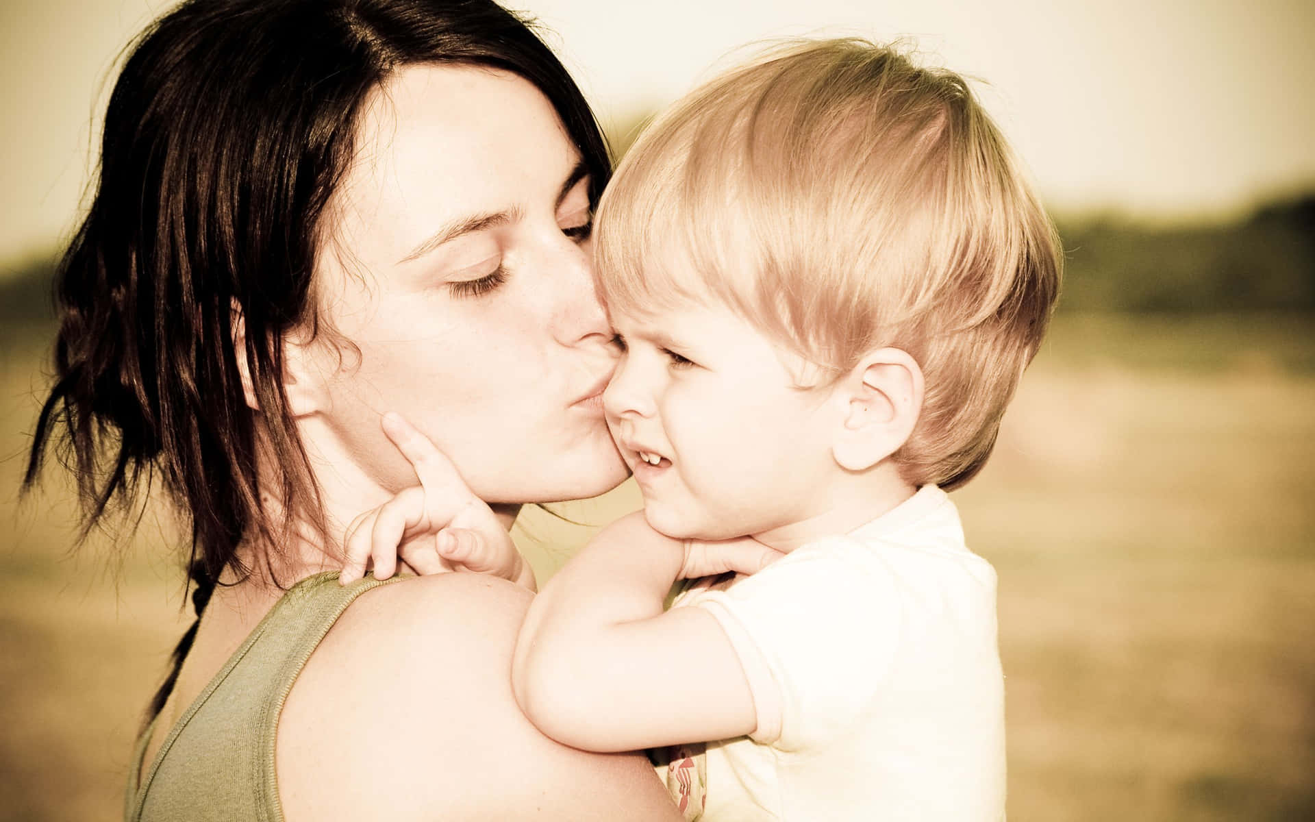 A Woman Kissing Her Child In A Field