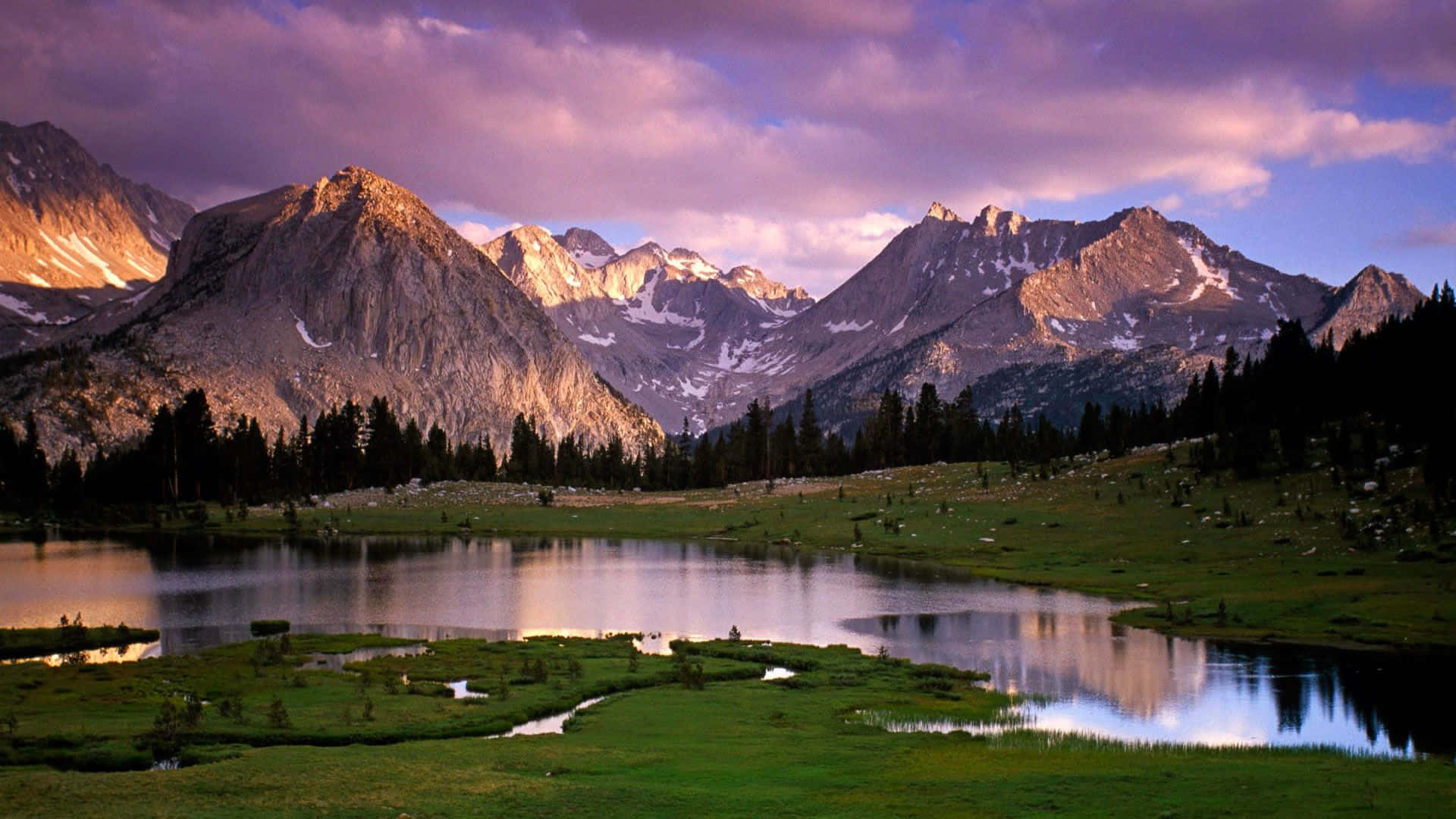 a lake surrounded by mountains and grass Wallpaper