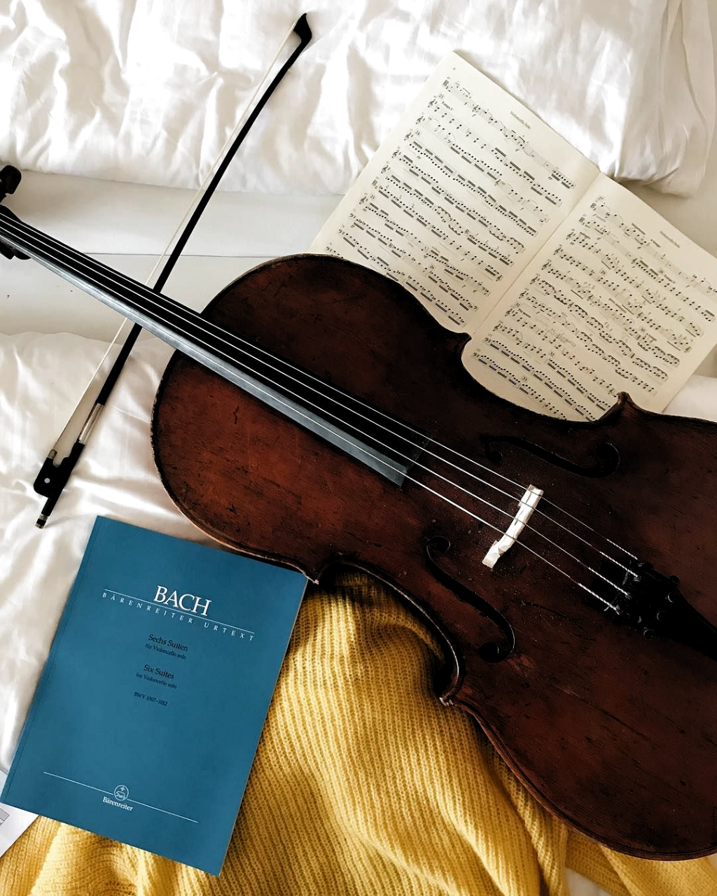 A Cello And Music Sheet On A Bed