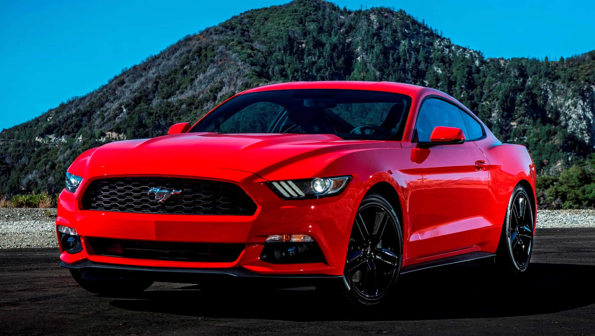 Den røde Ford Mustang er parkeret foran bjerge.