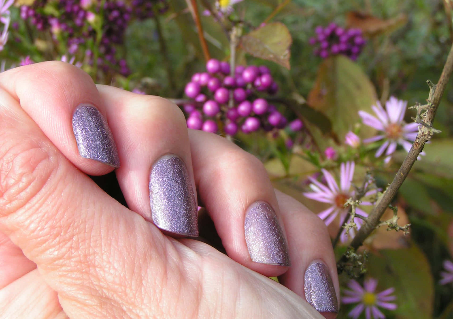 A Woman Holding A Purple Nail Polish In Front Of Flowers