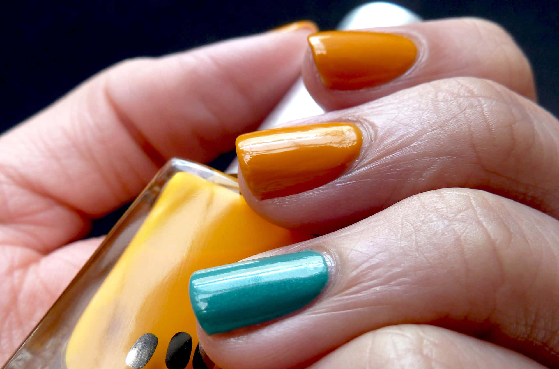 A Person Holding A Bottle Of Orange And Turquoise Nail Polish