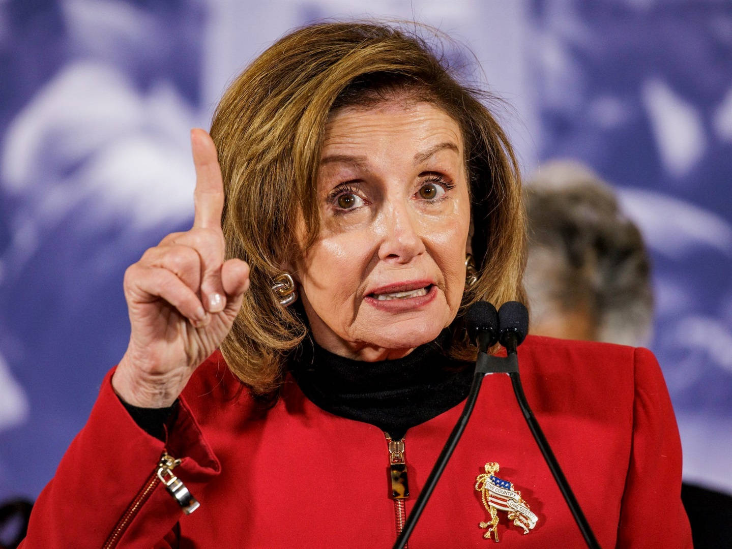 Caption: U.S. Speaker of the House, Nancy Pelosi, gesturing upward during a public event Wallpaper