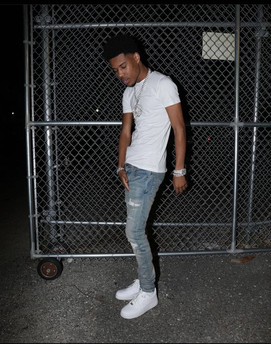 A Man In A White Shirt And Jeans Standing In Front Of A Fence Wallpaper