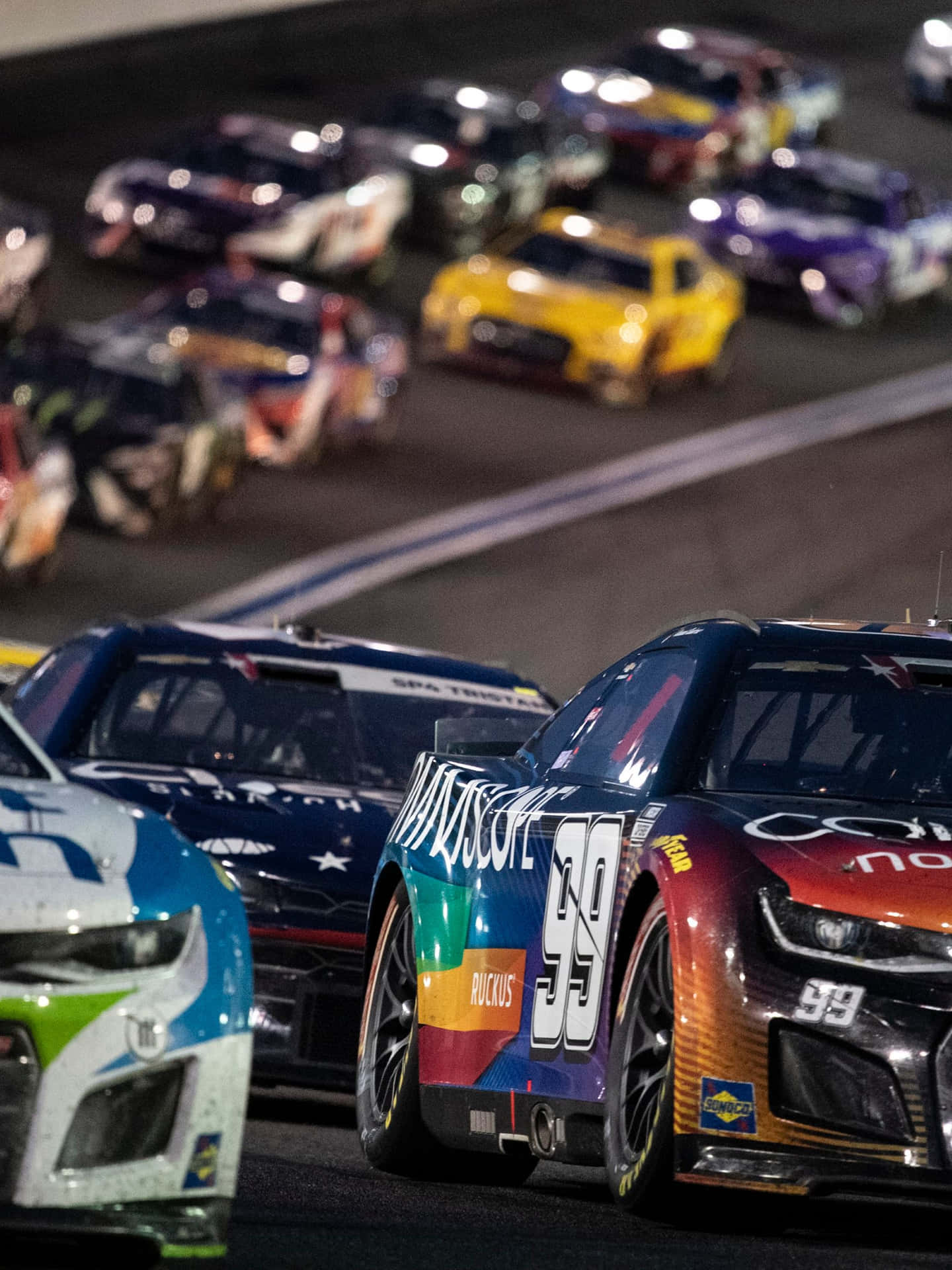 Nascar Races At Night With Cars In The Background Wallpaper
