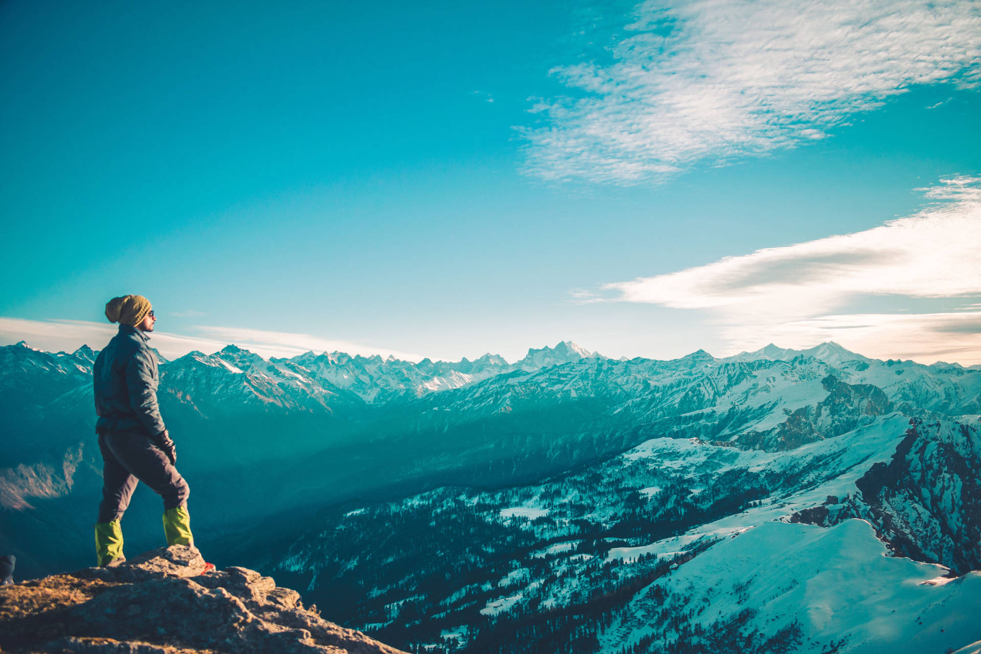 A Person Standing On Top Of A Mountain Looking At The Snowy Mountains Wallpaper