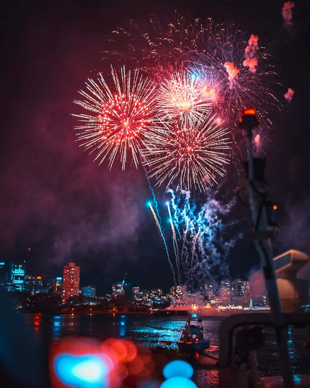 Fireworks Over A City With A Boat In The Background Wallpaper