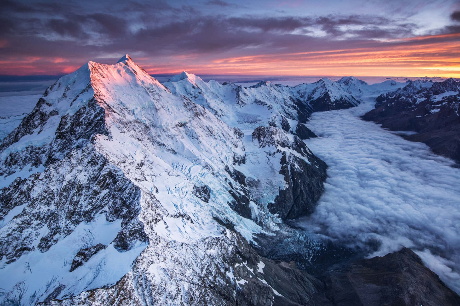 a mountain range with snow and clouds at sunset