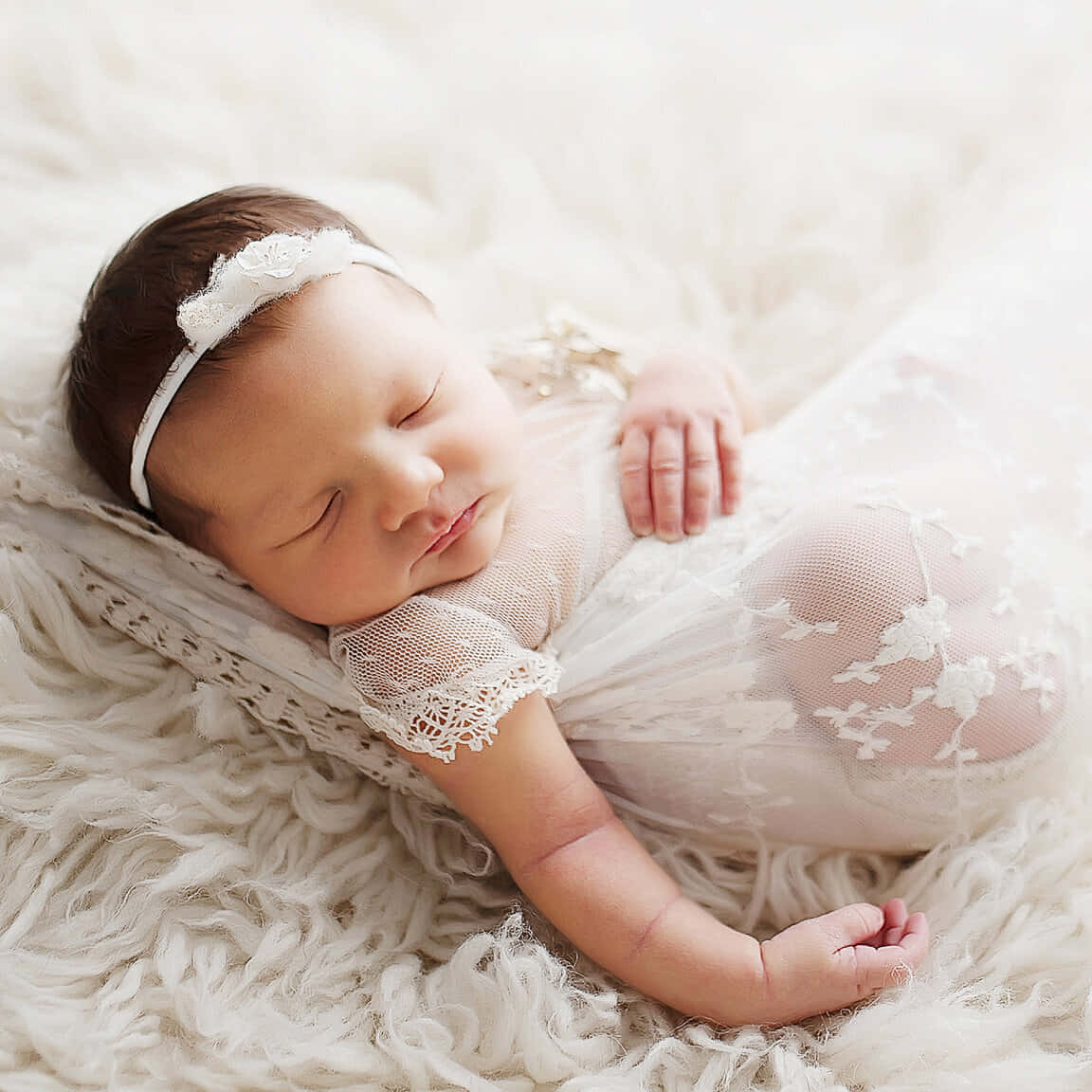 A Baby Girl Is Laying On A White Blanket