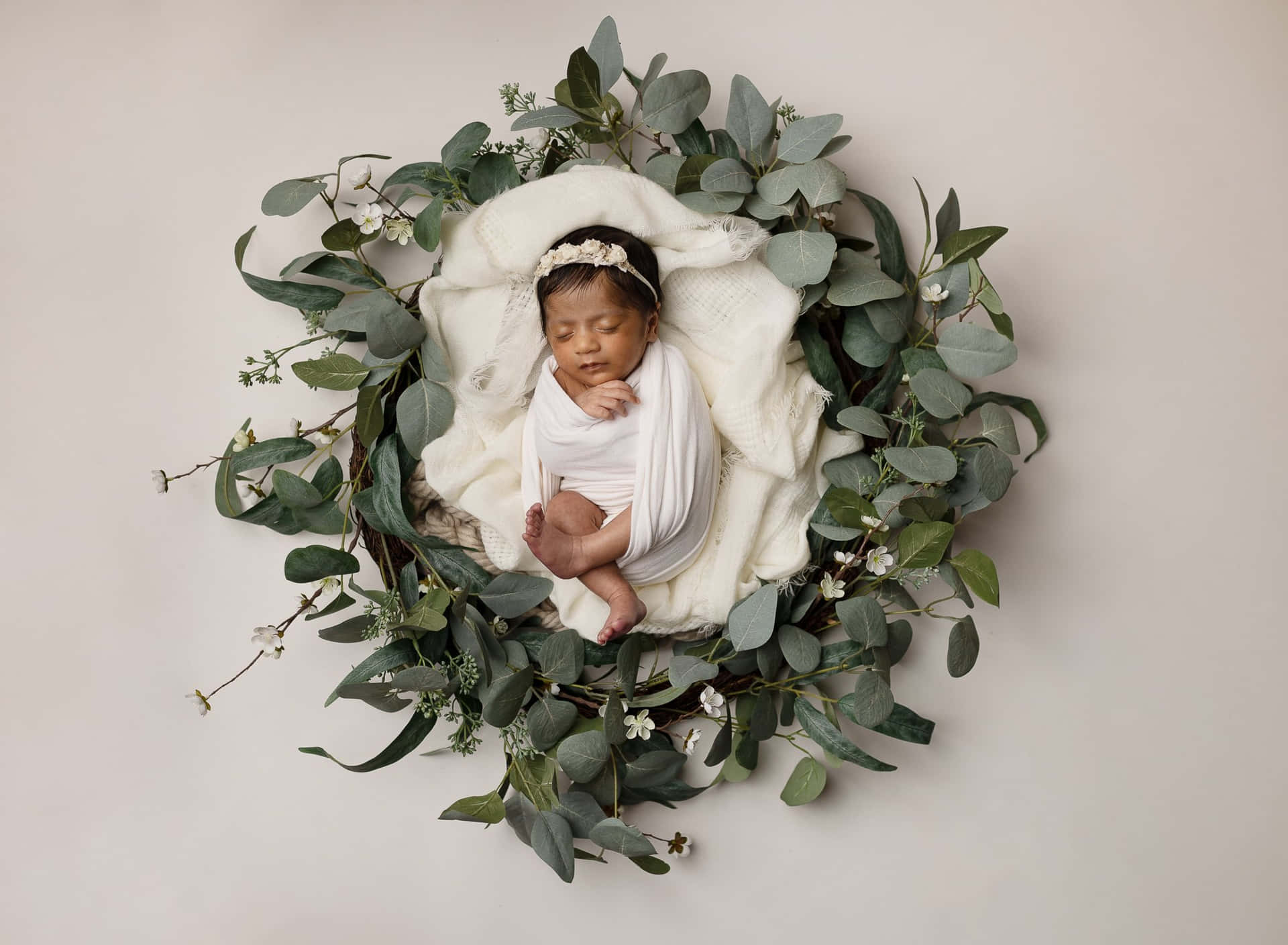 A Newborn Girl Is Laying In A Wreath Of Eucalyptus Leaves