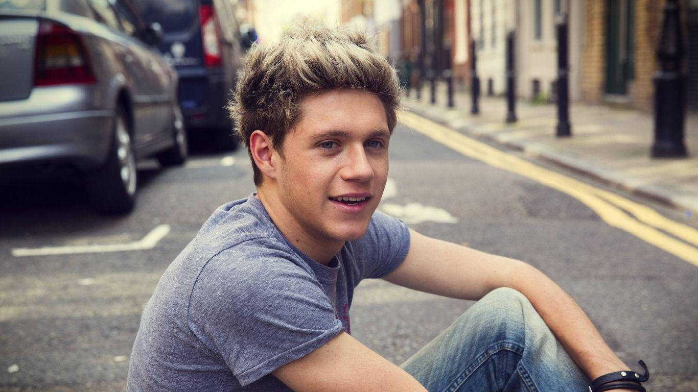 Niallhoran Sitter På Vägen. (this Could Be A Description Of A Wallpaper Image Featuring Niall Horan Sitting On A Road.) Wallpaper