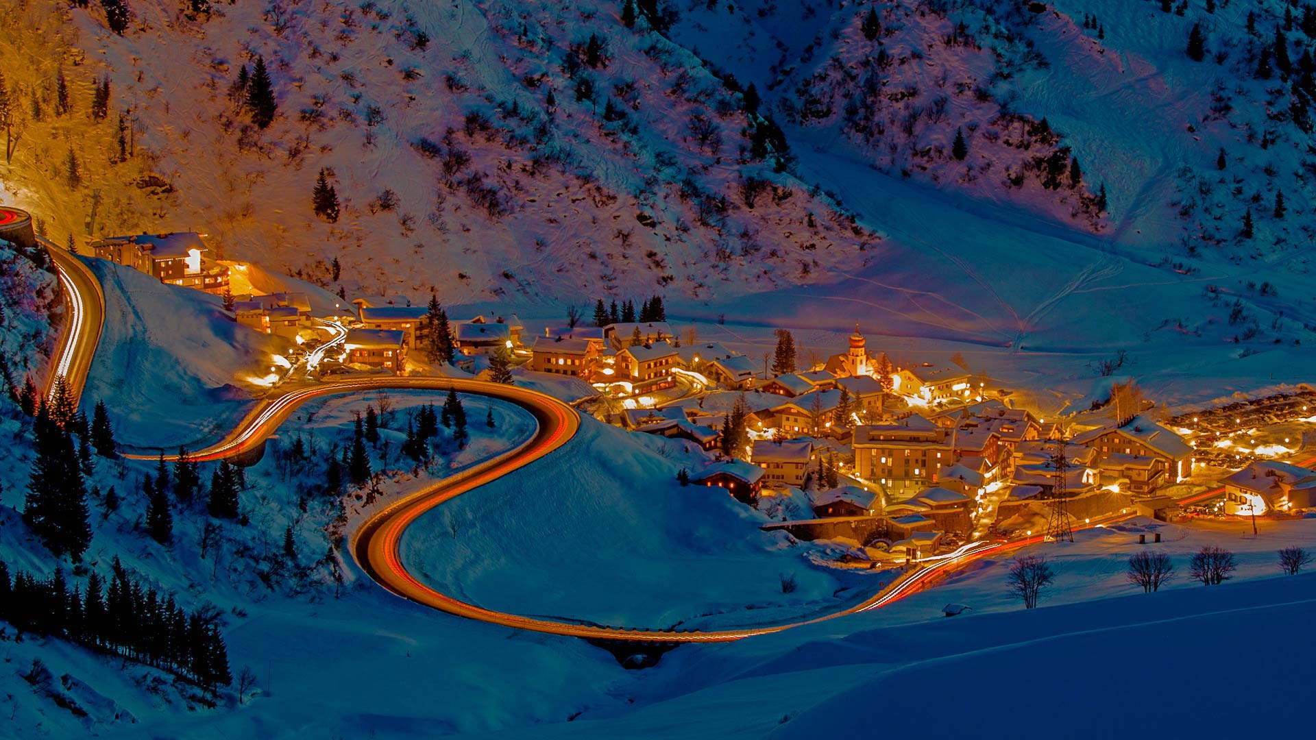 See the city lights reflecting on the snow-capped mountains with Bing Wallpaper