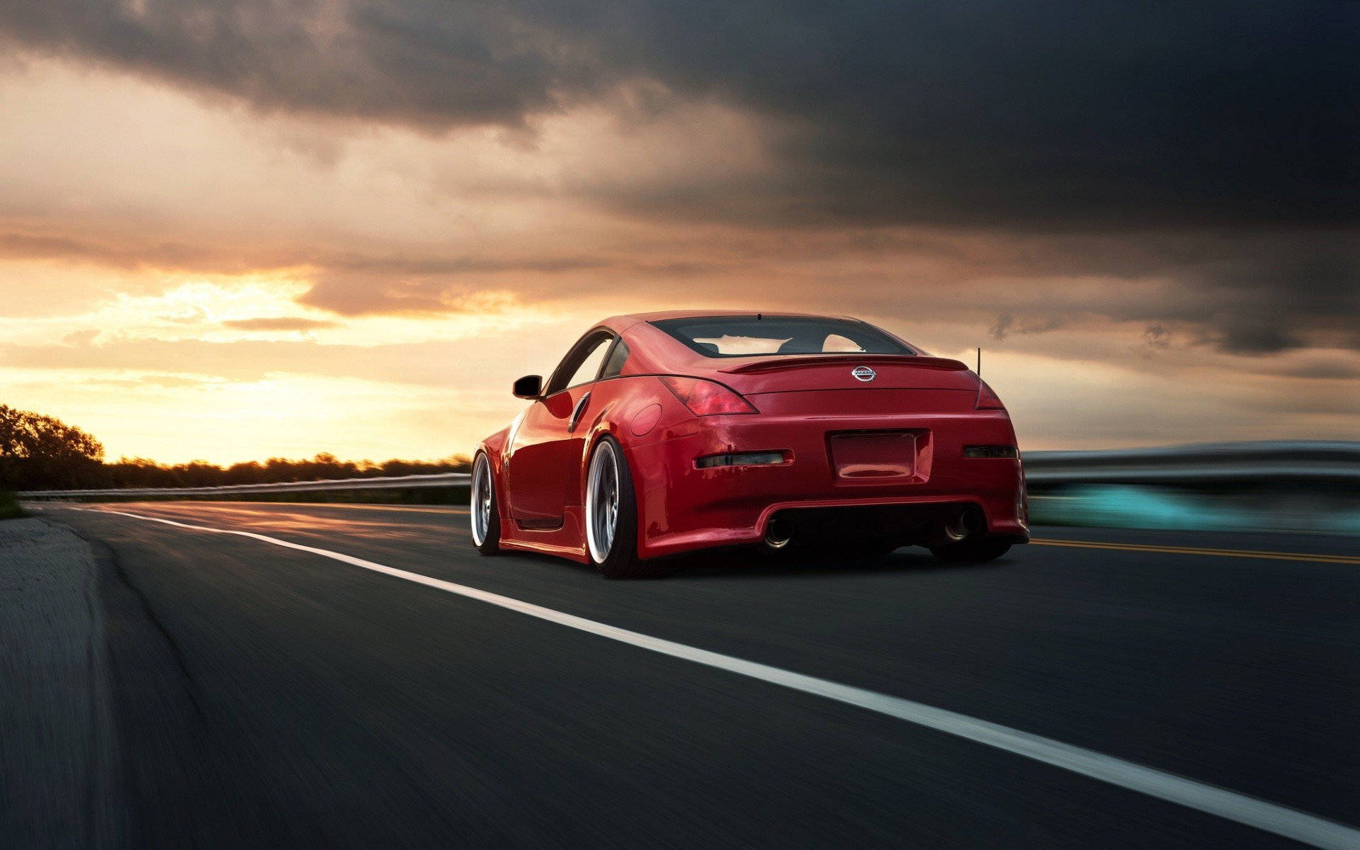 A Red Sports Car Driving Down A Road At Sunset Wallpaper