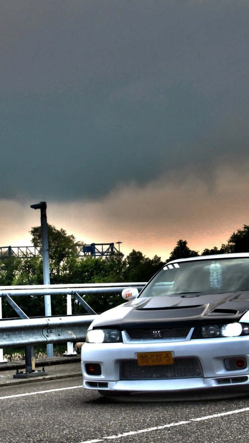 A White Car Driving On A Bridge Under A Cloudy Sky Wallpaper