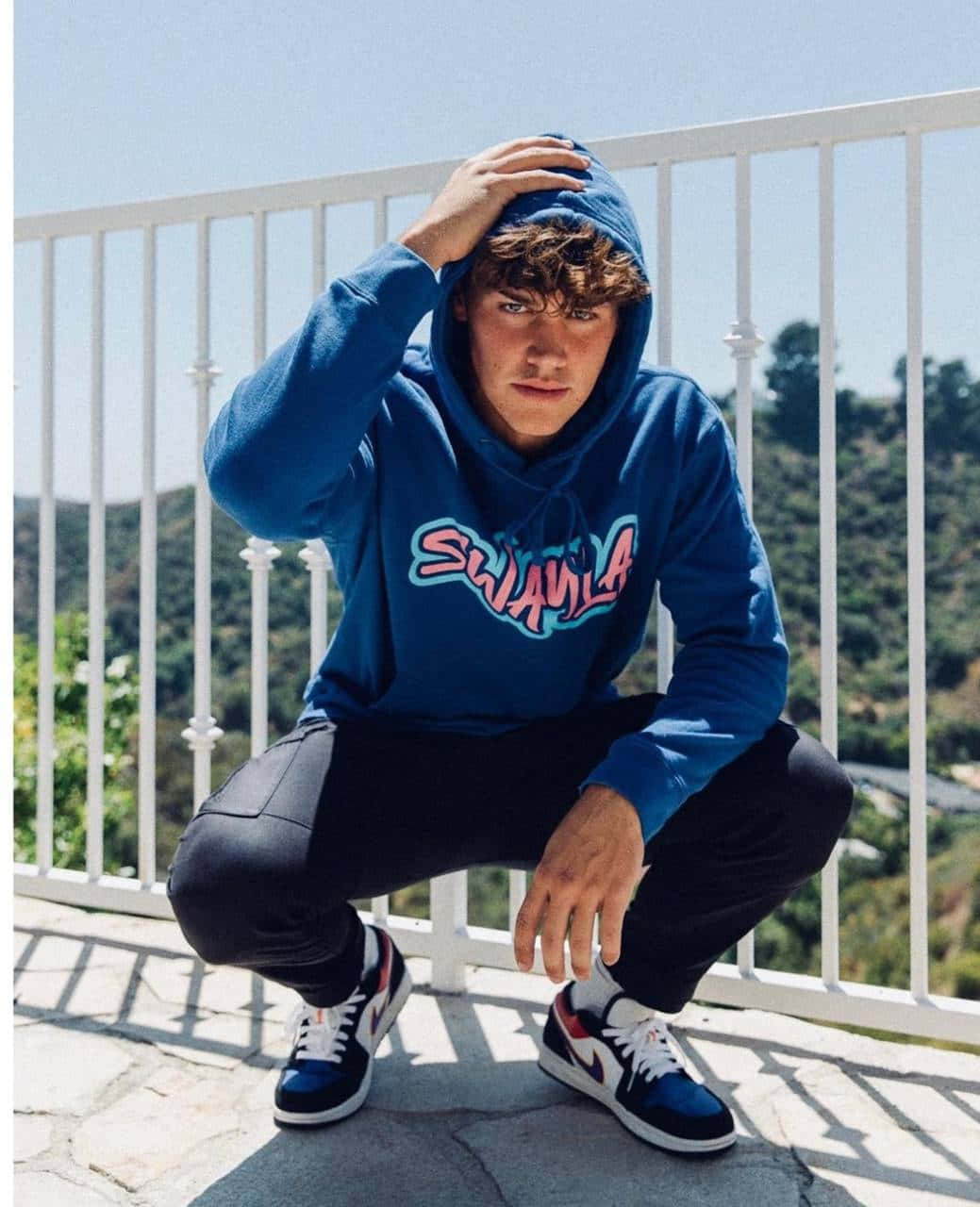 A Man In A Blue Hoodie Squatting On A Railing Wallpaper