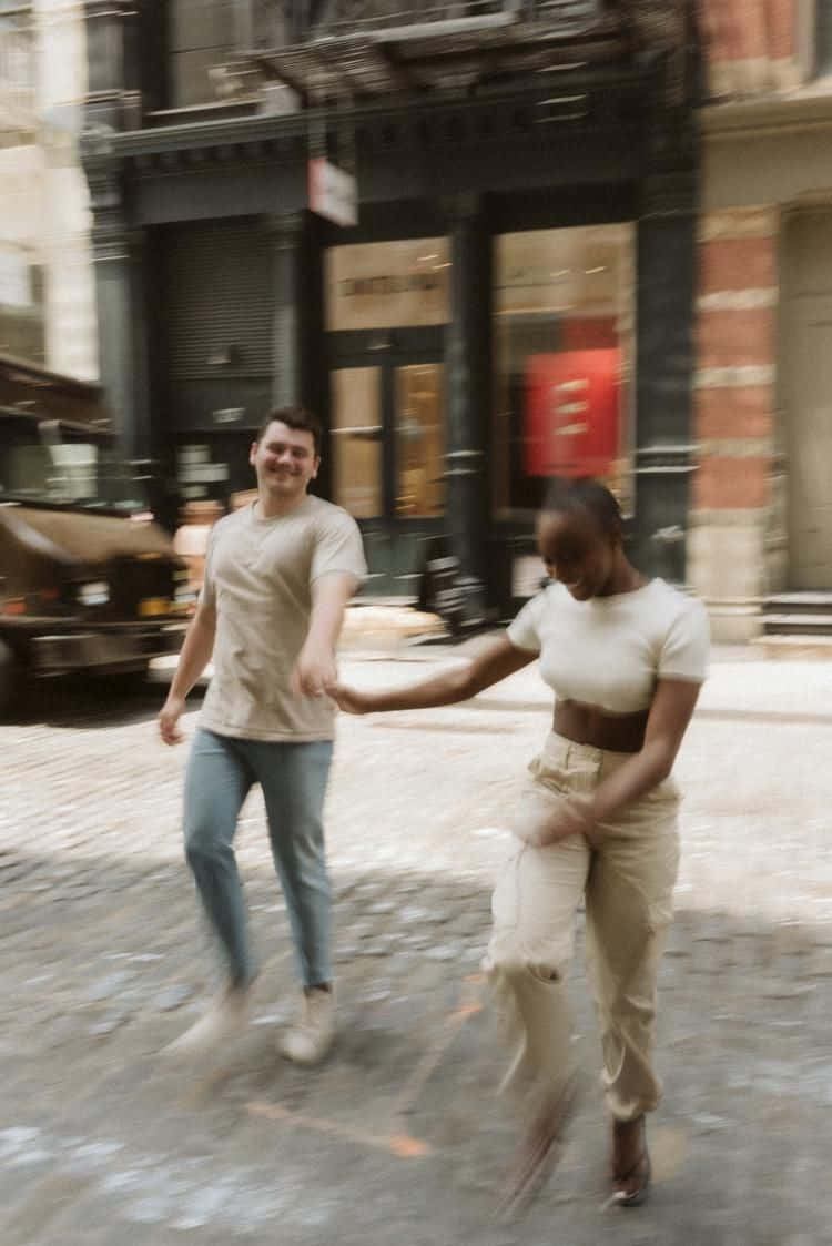 A Couple Is Walking Down A Street In A City