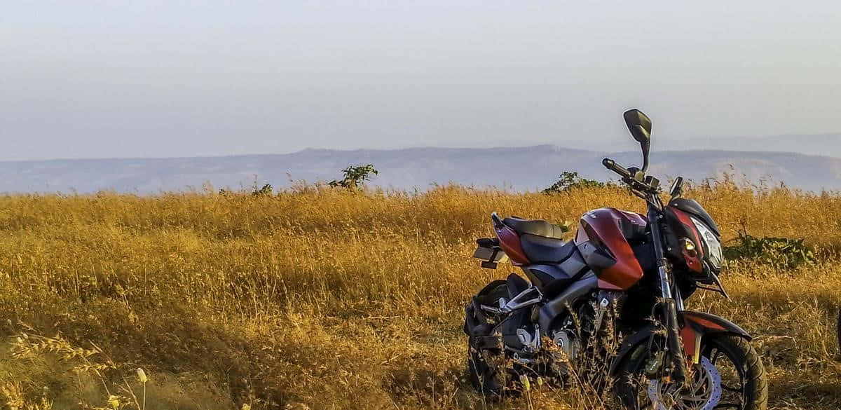 A Motorcycle Parked In A Field With A View Of The Mountains