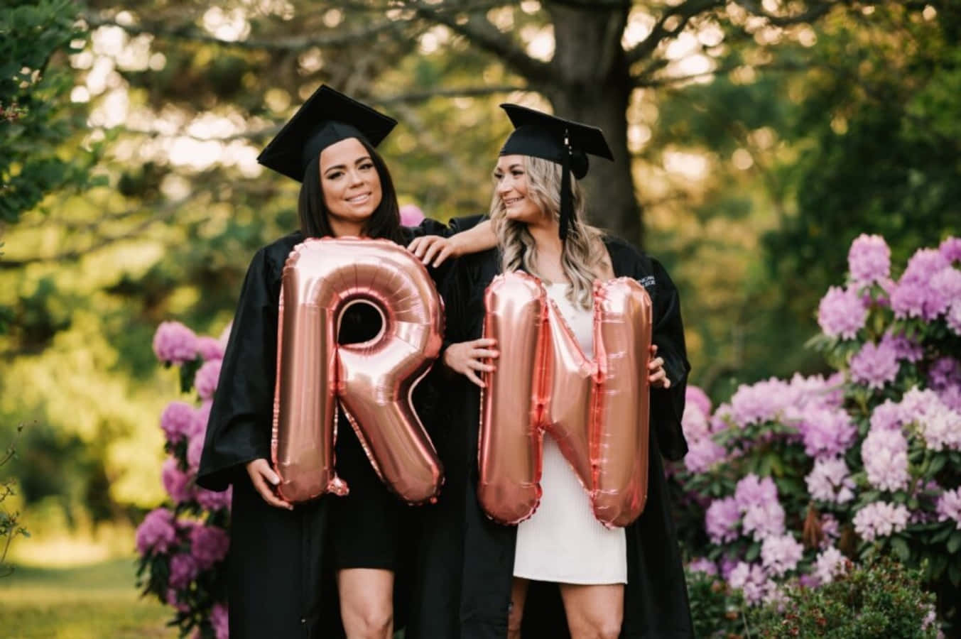 Two Women In Graduation Gowns Holding Balloons With The Letter R