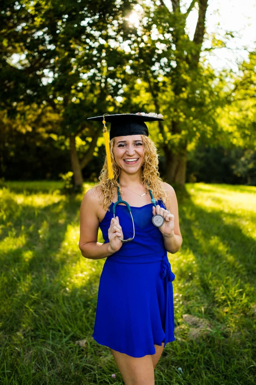 A Young Woman In A Blue Dress And Graduation Cap Poses For A Photo