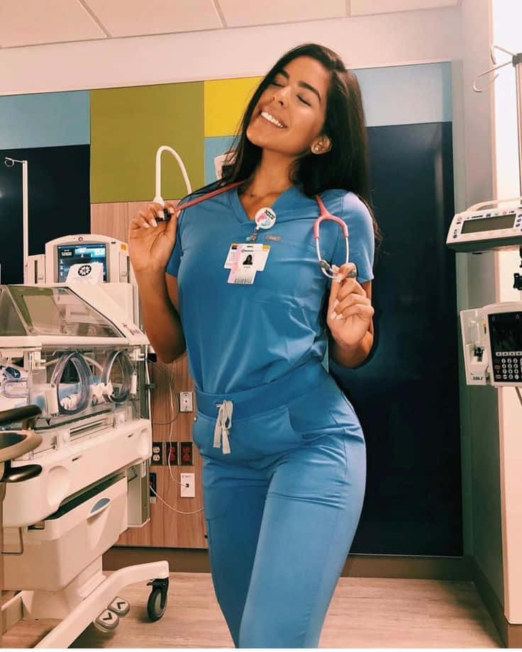 A Woman In Blue Scrubs Standing In Front Of A Bed
