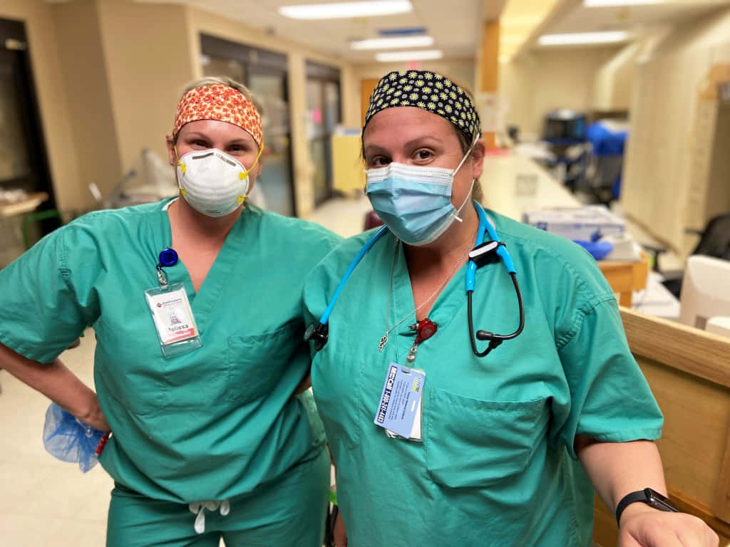 Two Nurses In Scrubs Standing In A Hospital Hallway