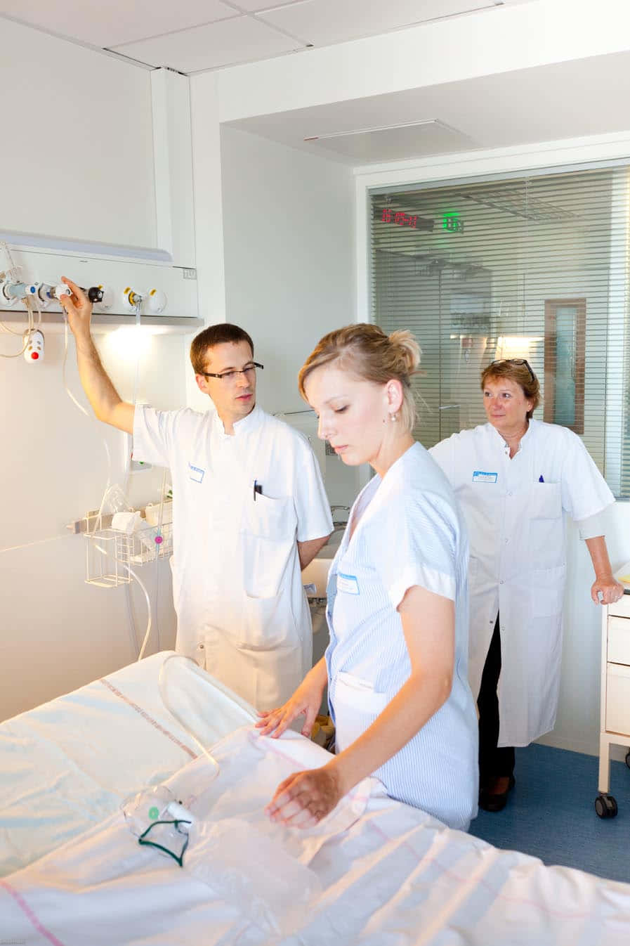 A Group Of People Standing Around A Bed In A Hospital