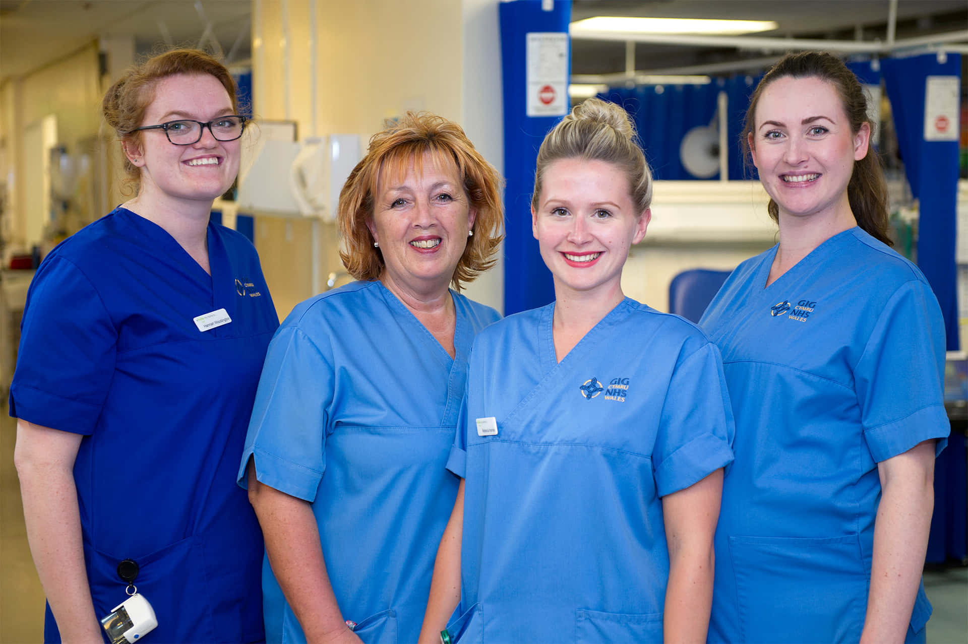 Four Nurses In Blue Scrubs Standing In A Hospital Corridor