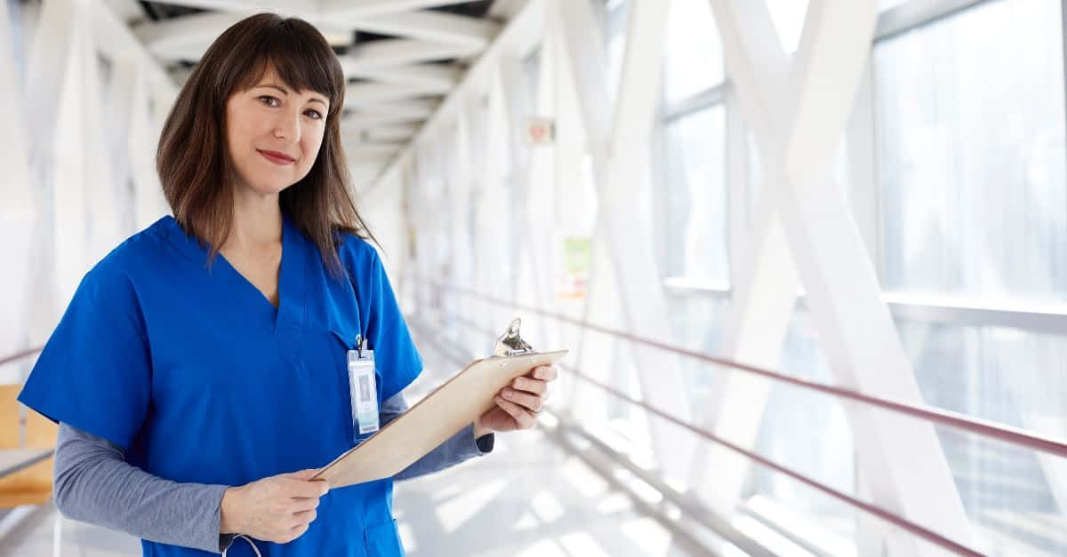 A Nurse Holding A Clipboard In A Hallway