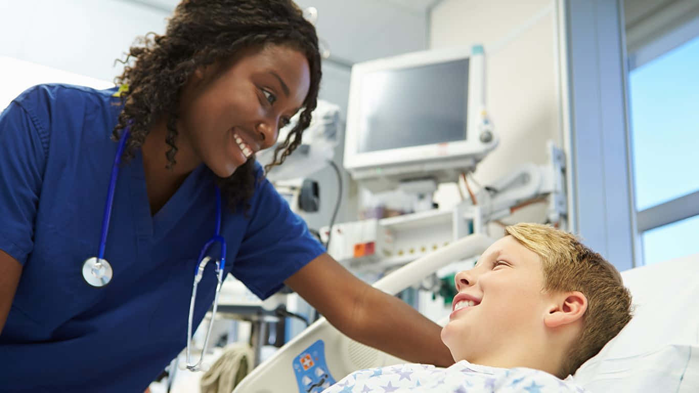 A Nurse Is Smiling At A Young Boy In A Hospital Bed