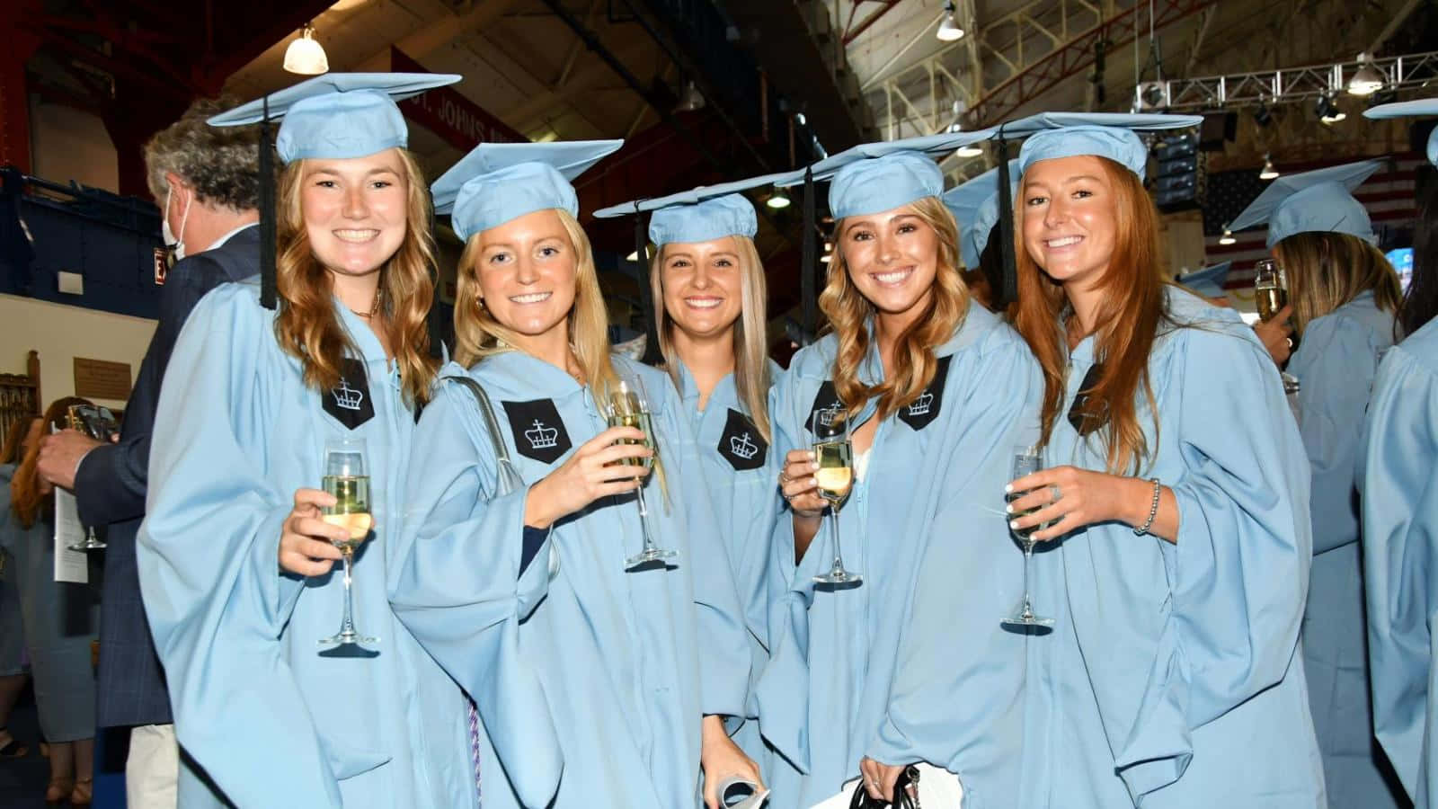 A Group Of Women In Blue Graduation Gowns Holding Champagne Glasses