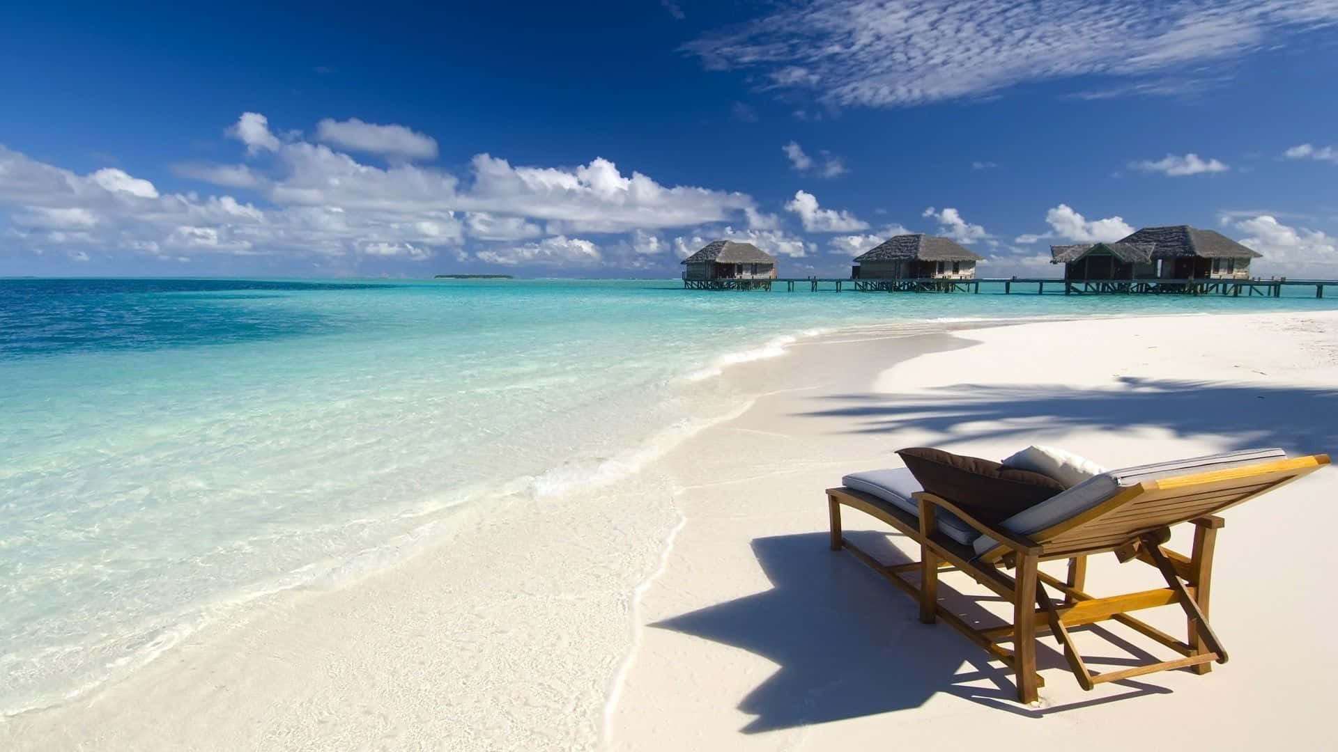 A Lounge Chair On A Beach With A Hut In The Background Wallpaper