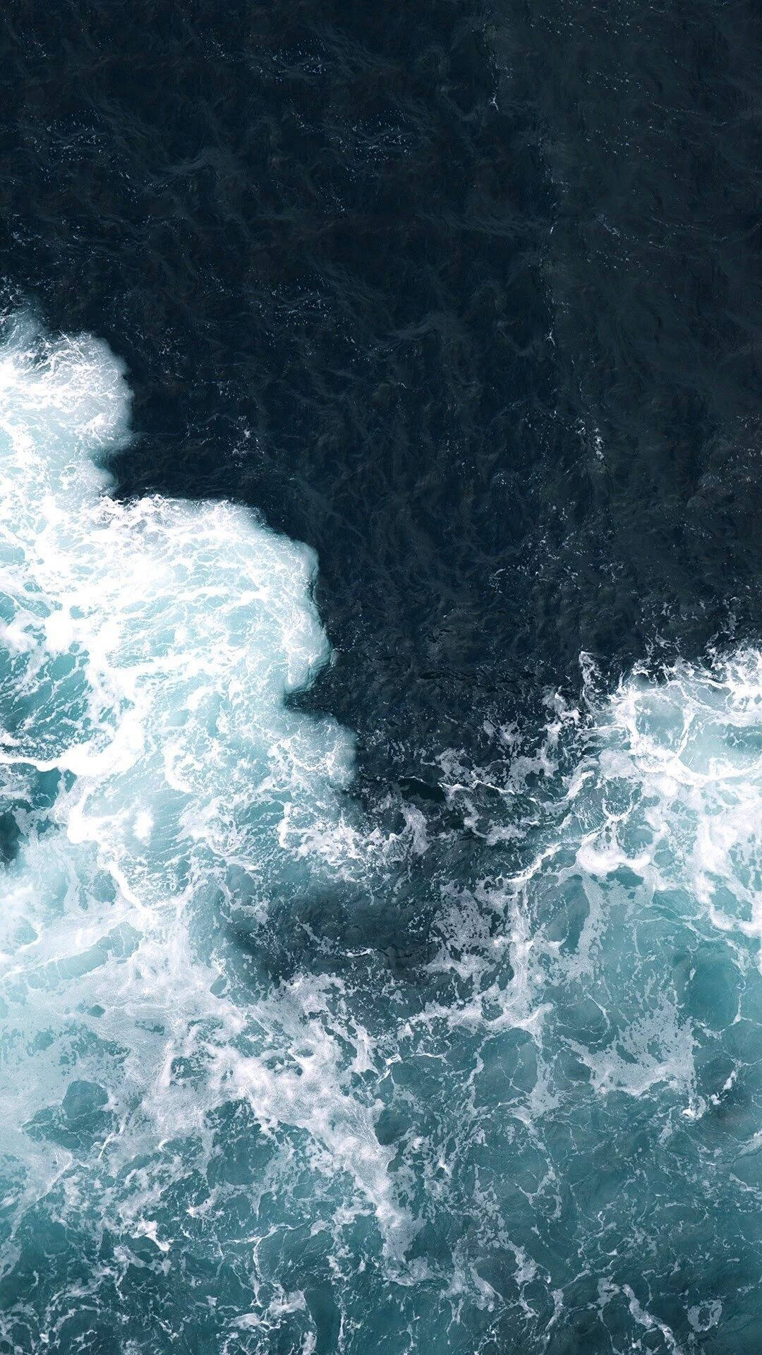 An aerial view of the power of ocean waves crashing against the shore. Wallpaper
