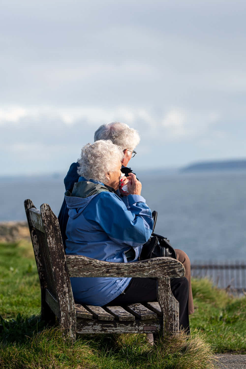 Unwavering Love: An Elderly Couple Relaxing on a Wooden Bench Wallpaper