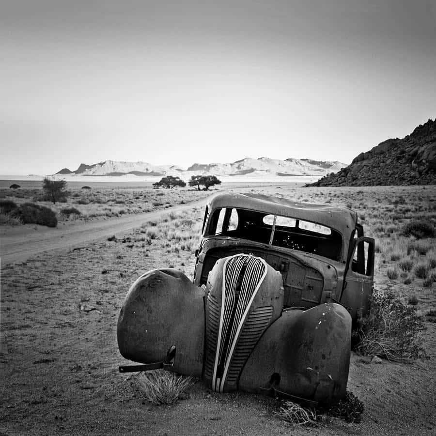 A Black And White Photograph Of An Old Car In The Desert