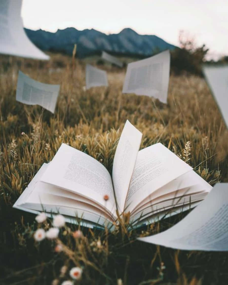 Open Book In The Grass With Paper Flying Around