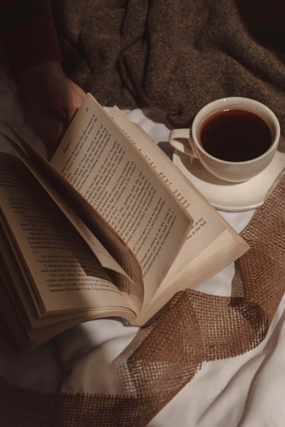 A Person Is Reading A Book And Drinking Coffee