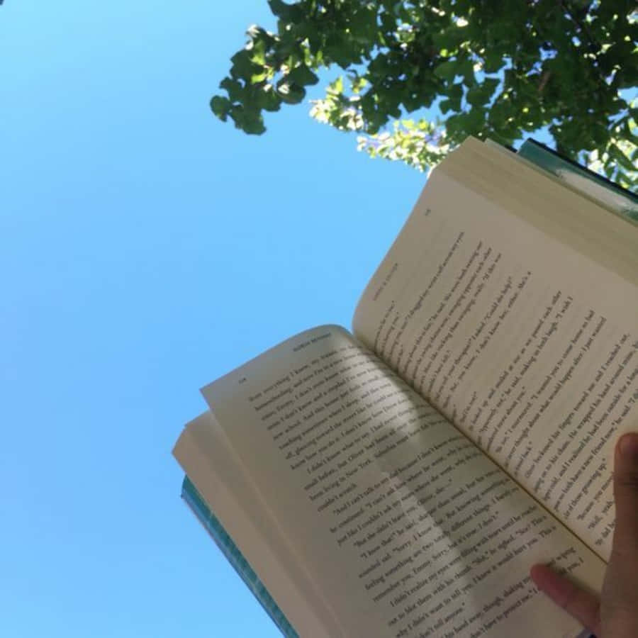 A Person Holding A Book Up To The Sky