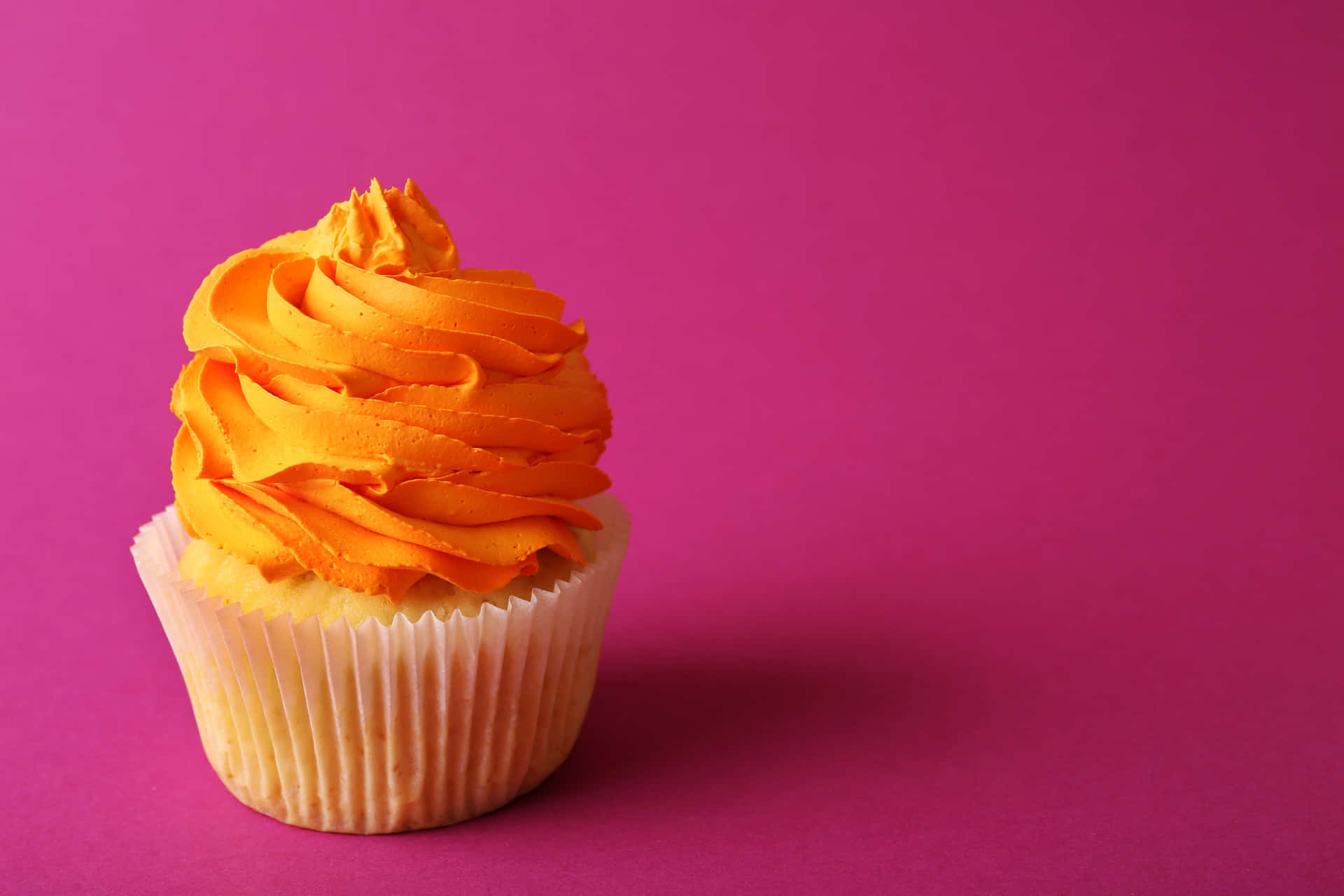 Orange Frosted Cupcakeon Pink Background Wallpaper