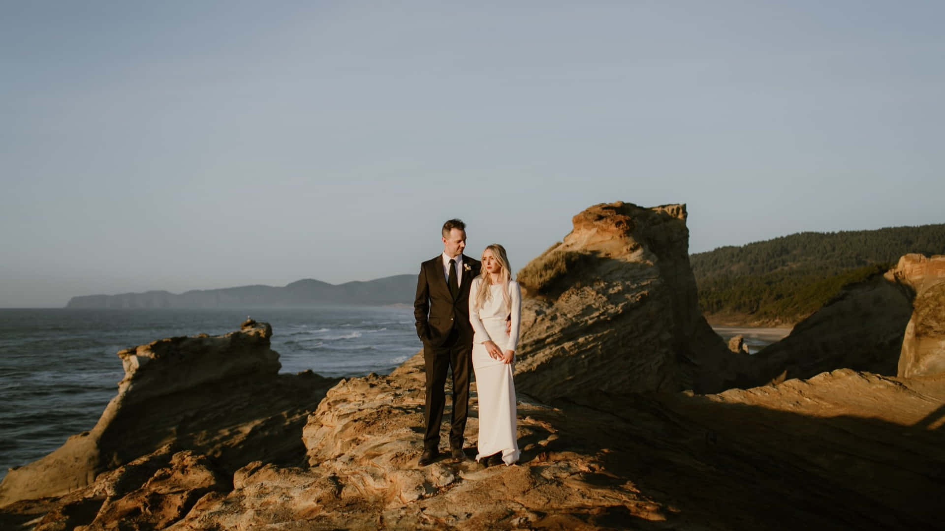 A Bride And Groom Standing On A Rock In Front Of The Ocean