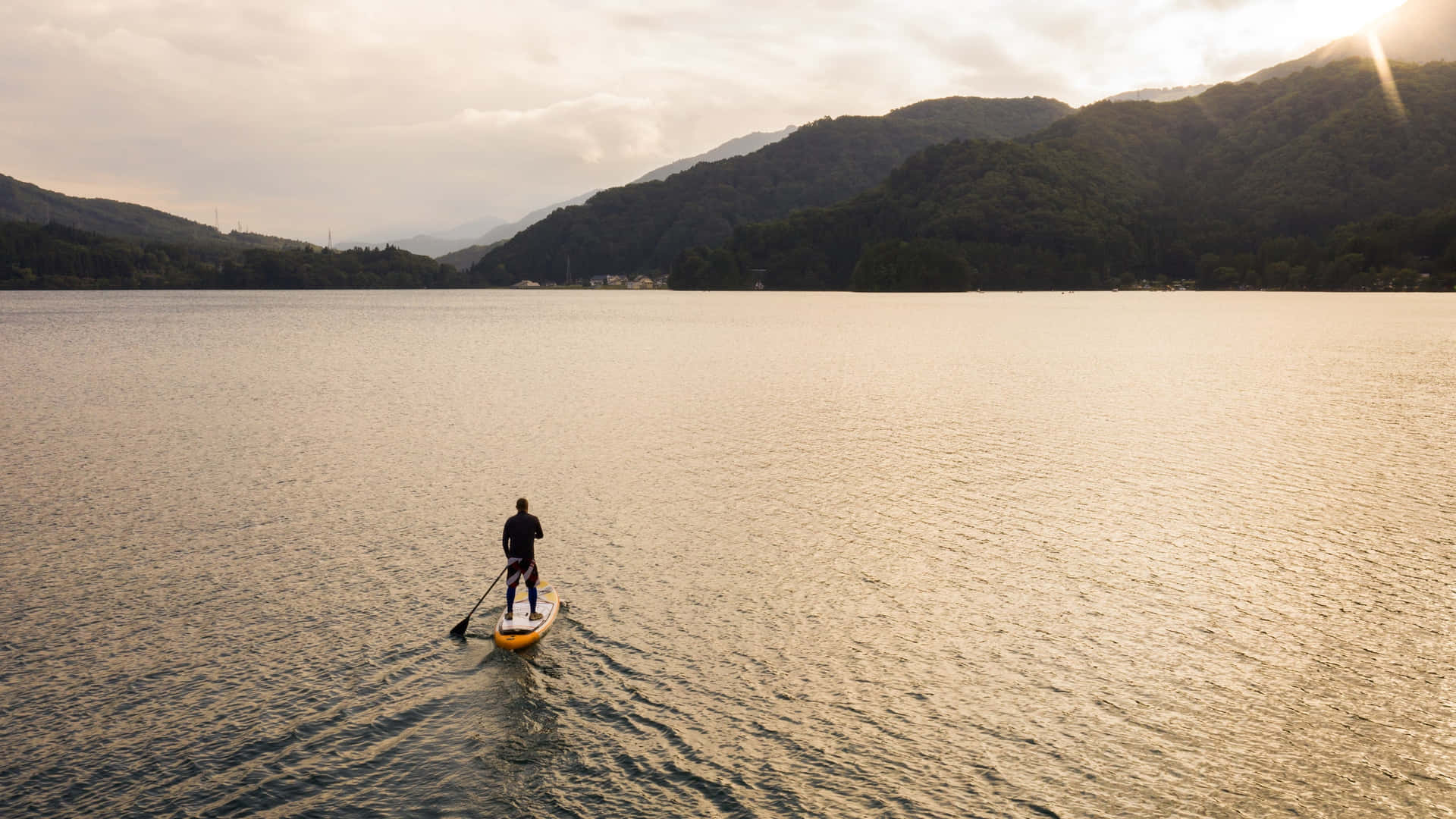 Paddleboarder enjoying a serene ride on a beautiful lake Wallpaper