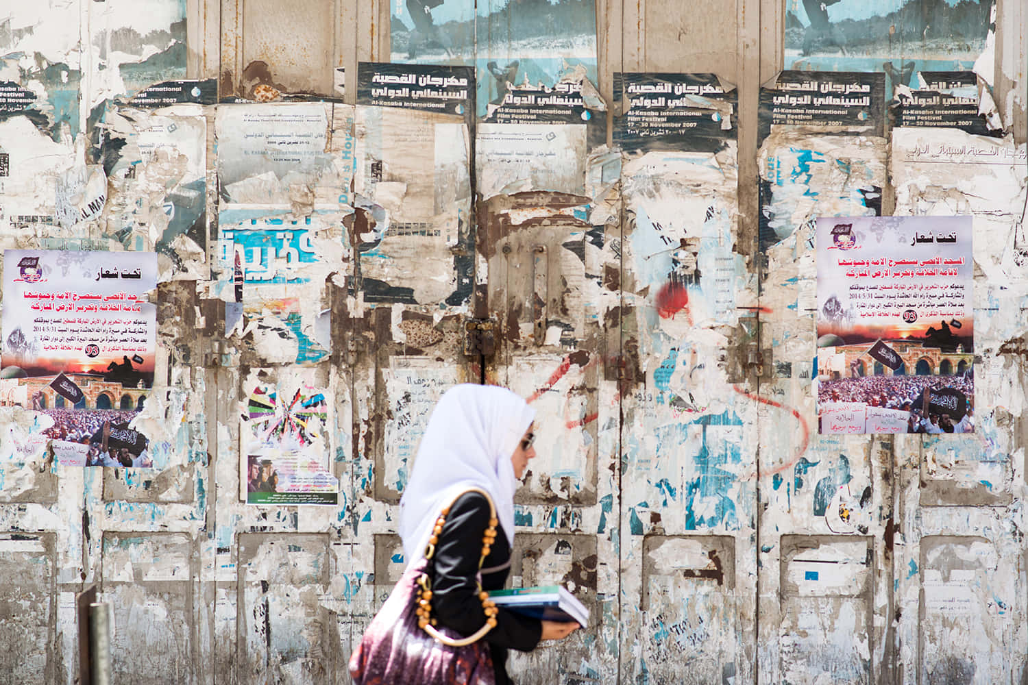 A Woman Walking Past A Wall With Posters