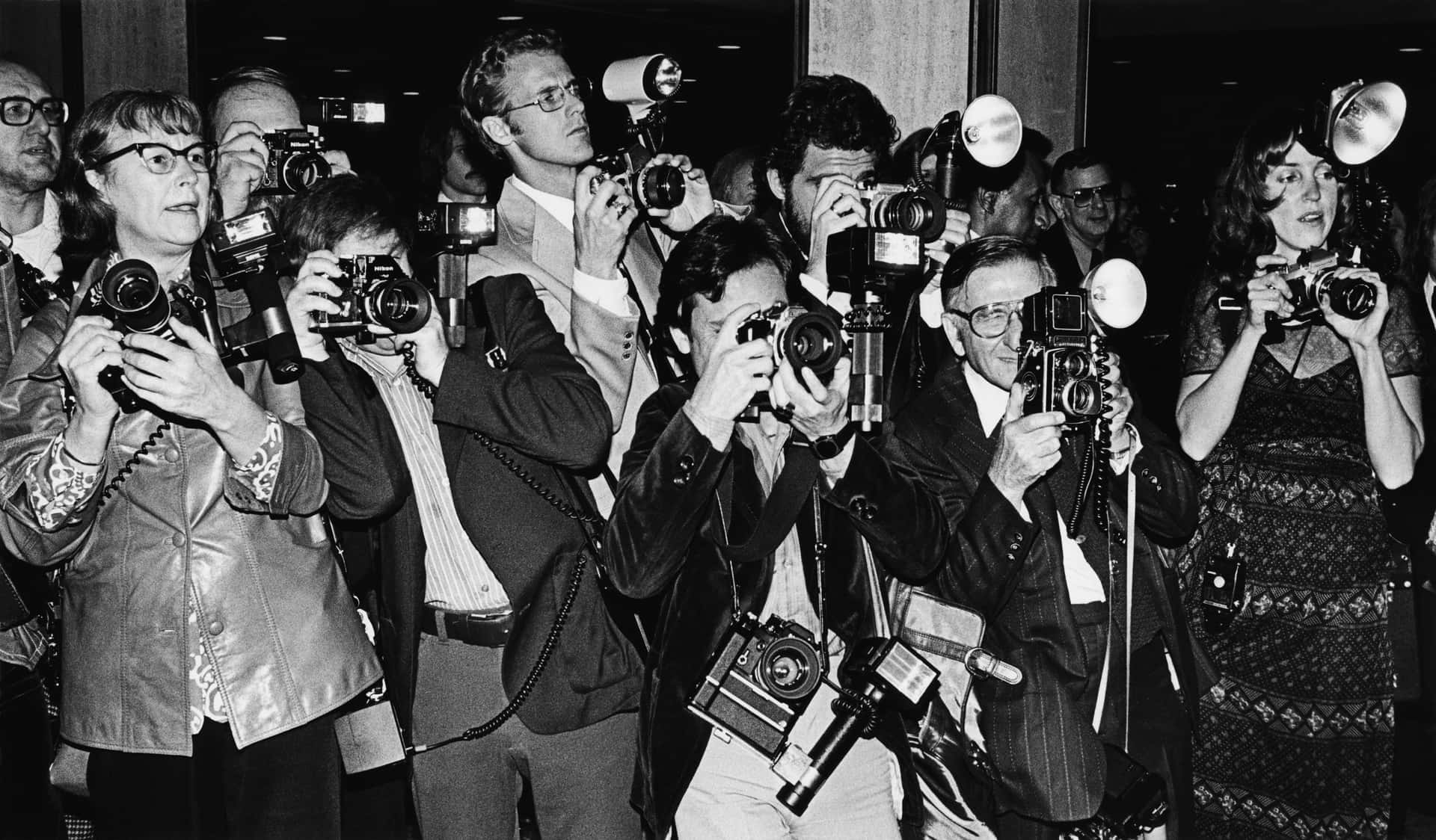 A Group Of People Holding Cameras In Front Of A Building Wallpaper