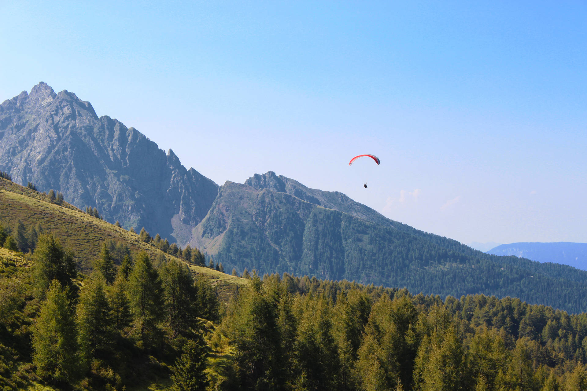 Paraglidingüber Bewaldeten Hügeln Wallpaper
