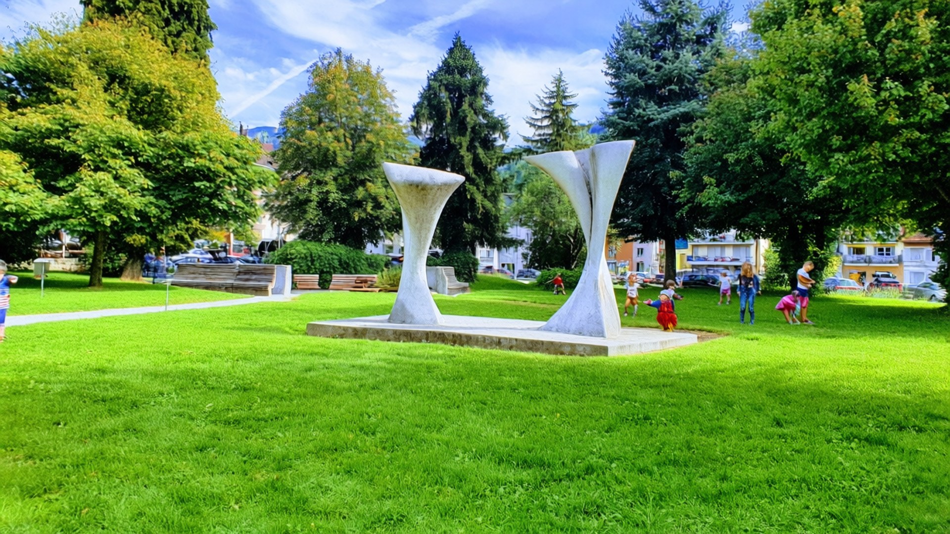 Eine fröhliche Parkszene in Yverdon-les-Bains mit einer modernen Skulptur und spielenden Kindern.