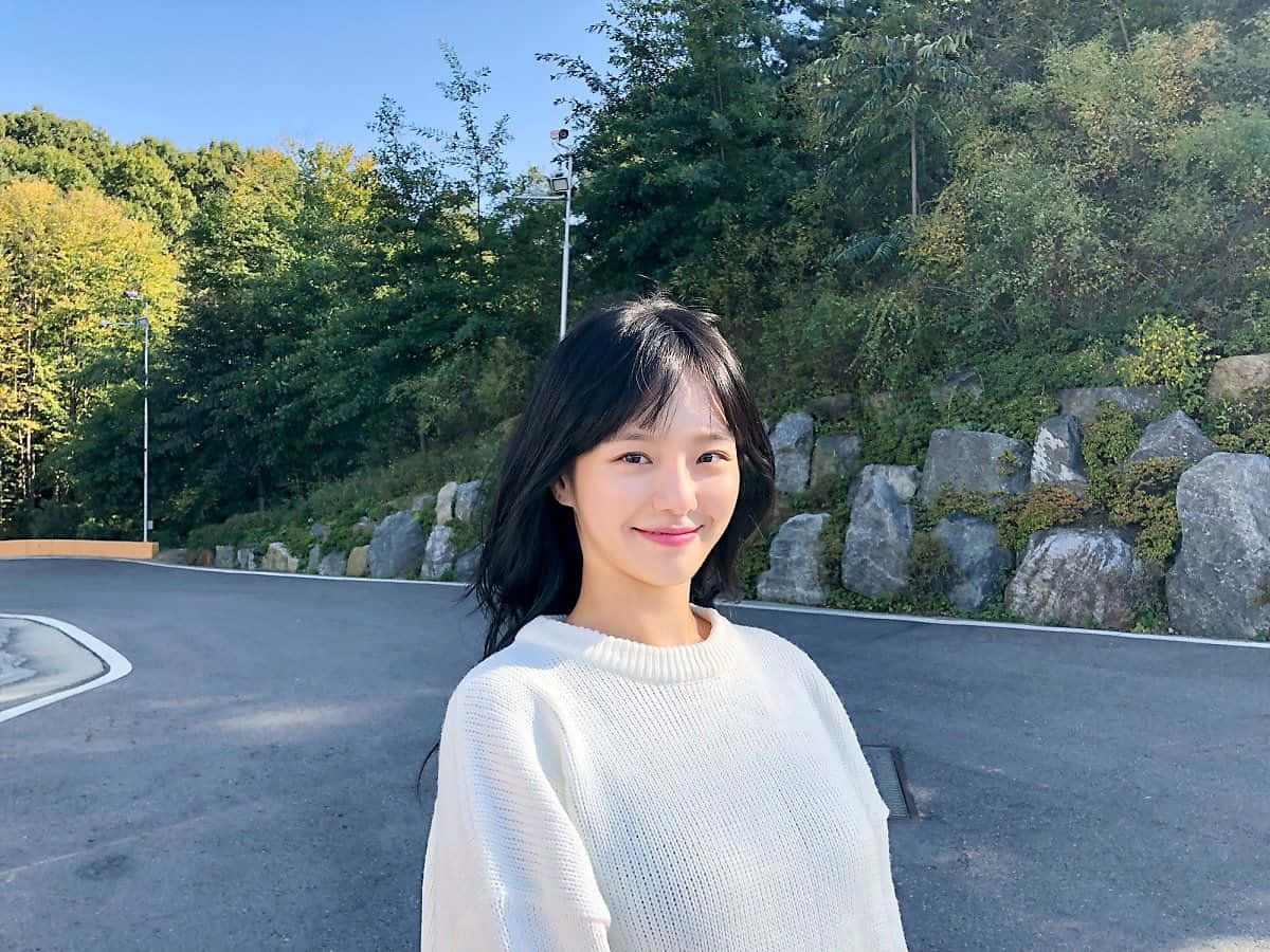 A Woman In A White Sweater Standing In Front Of A Road Wallpaper